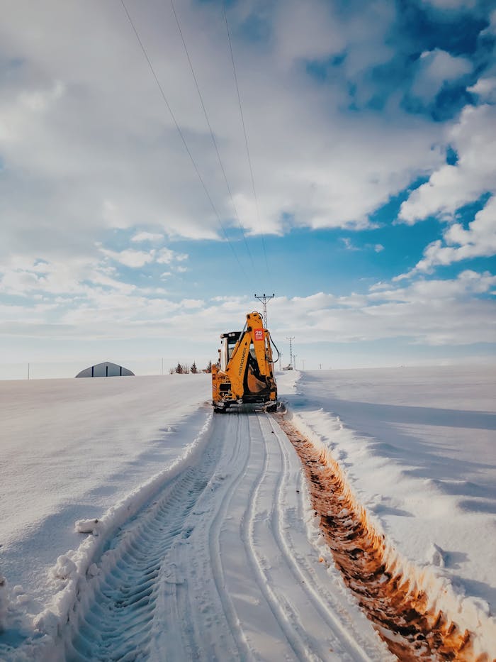 A bulldozer plowing through heavy snow under a bright blue sky in a winter setting.